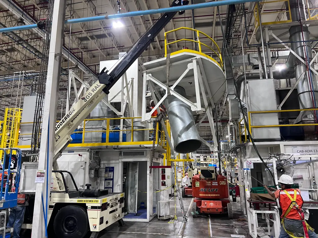 Izaje de una tolva sobre una máquina con grúa dentro de la planta